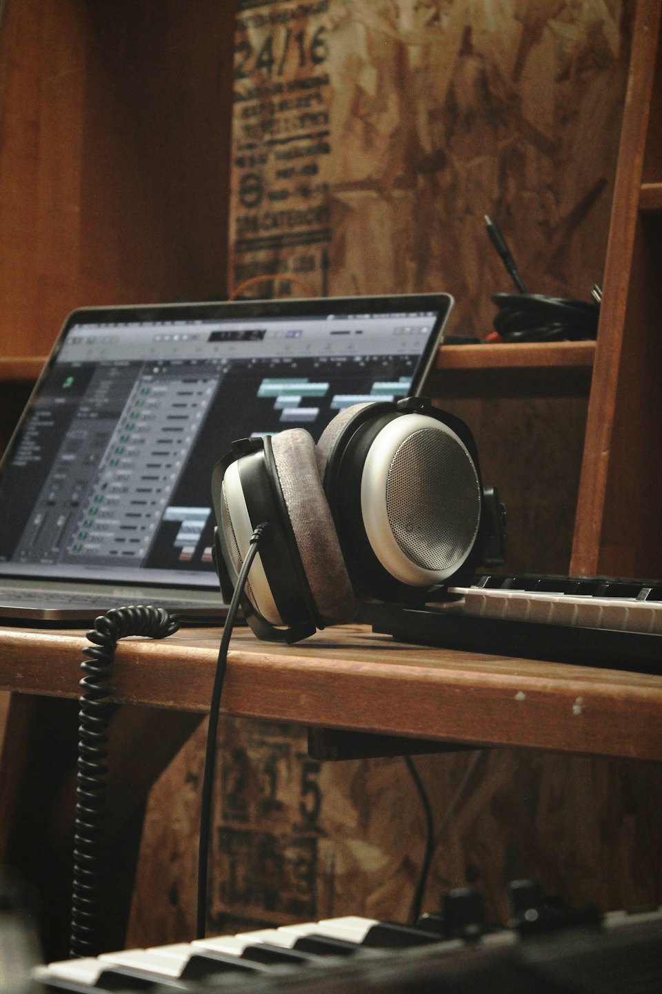 Silberner Laptop mit Audio-Software, Kopfhörern und MIDI-Keyboards auf einem Holztisch.