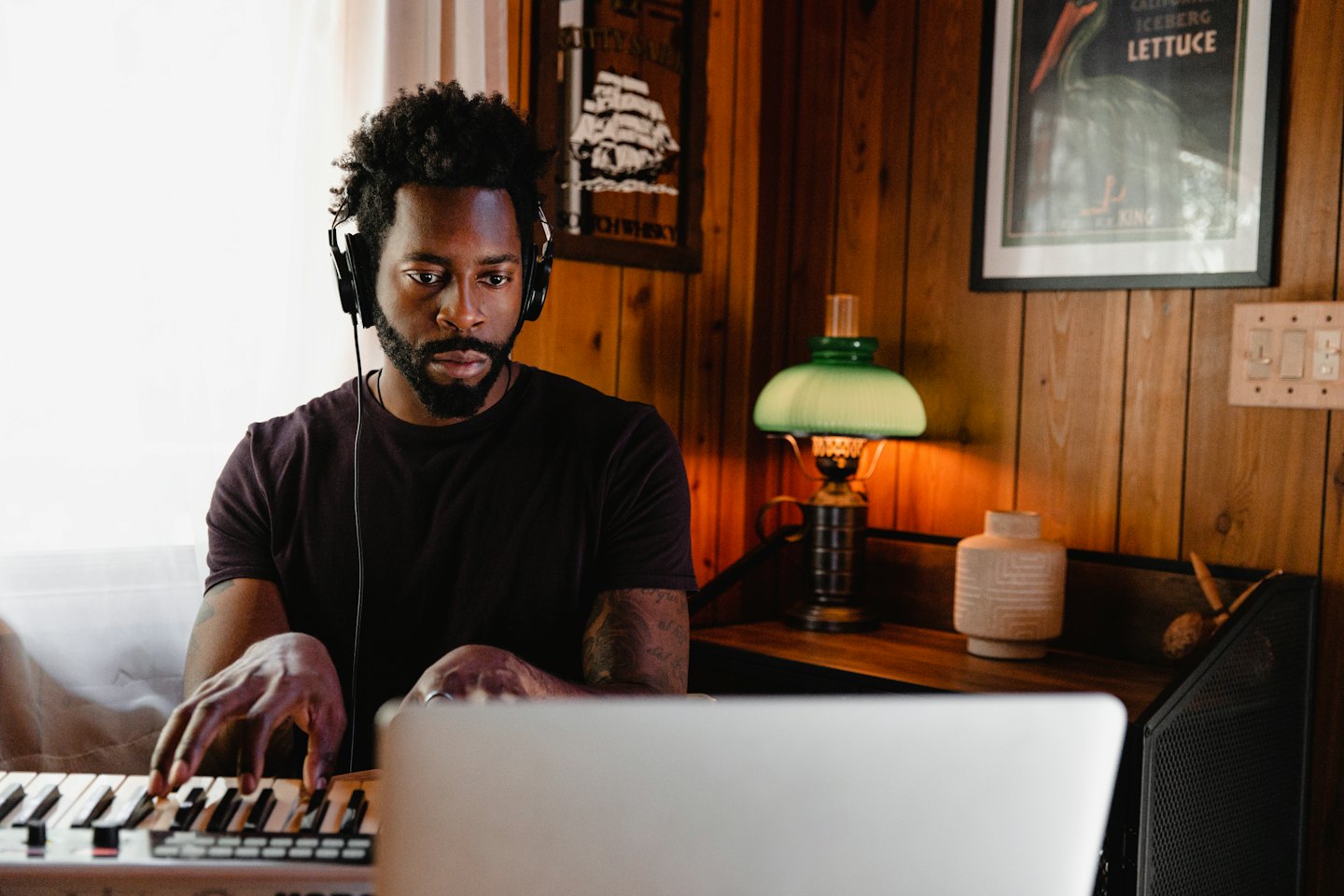 Ein Mann mit Kopfhörern spielt auf einem MIDI-Keyboard und schaut auf einen Laptop.